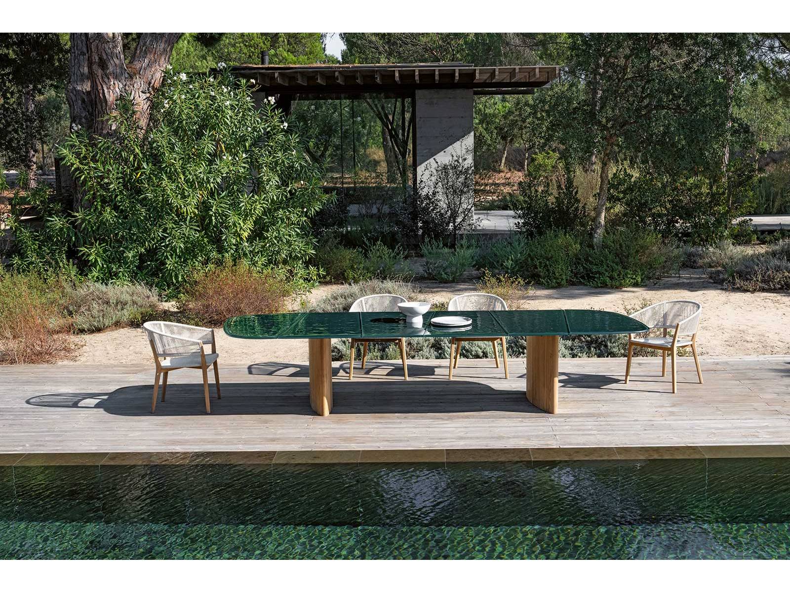 Der Tisch «Regaliz» von Kris Van Puyvelde feiert den Luxus unter freiem Himmel. Seine Glasplatte, kunstvoll verschmolzen und in edlen Farbtönen wie Dunkelgrün, -braun oder Pebble schimmernd, fängt das Licht ein wie eine Bühne. Darunter: massive Beine aus Teak.  ROYAL BOTANIA.