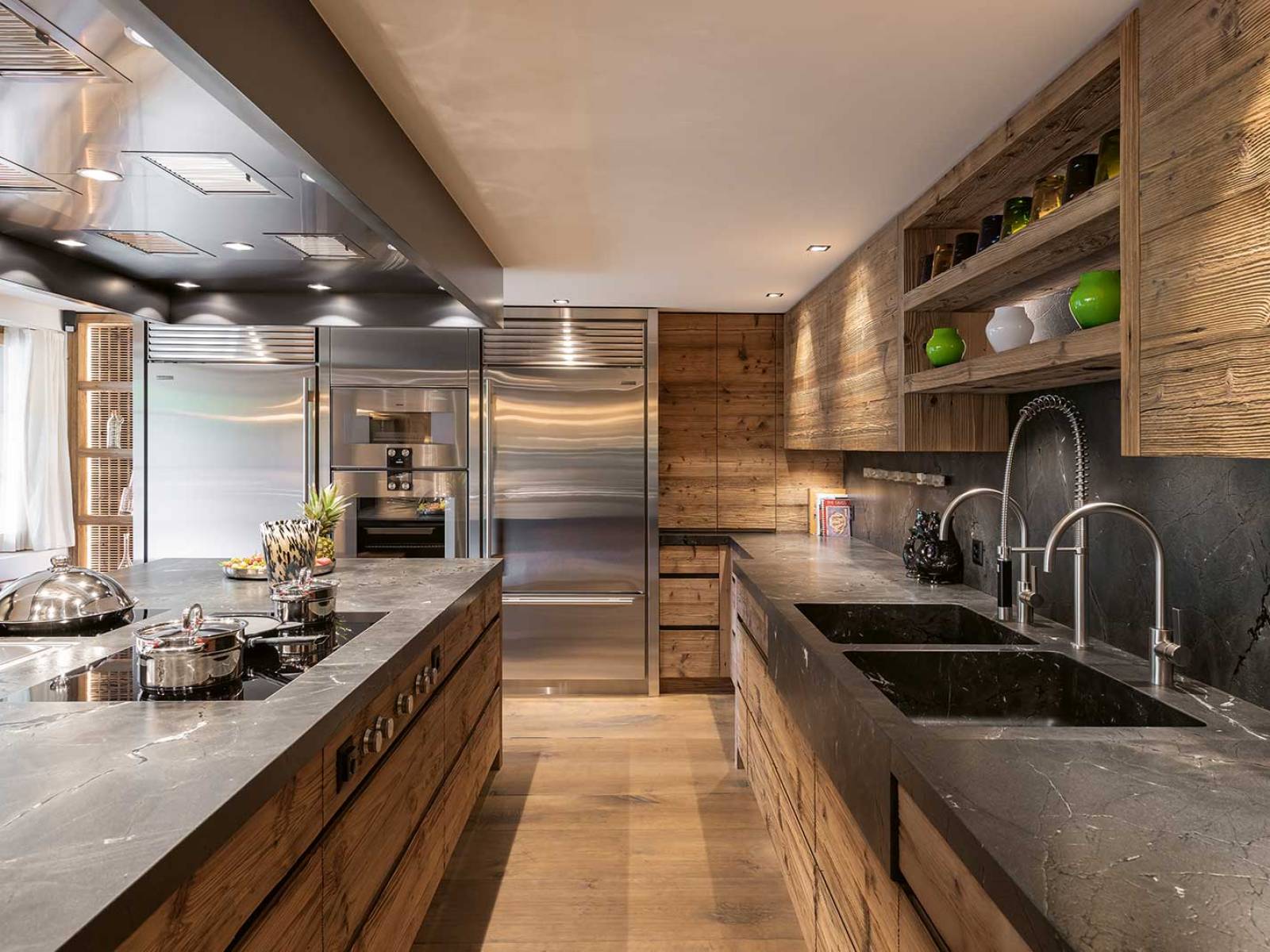 Handwerk und Material verschmelzen in dieser Küche zu einer stimmigen Einheit: In sorgfältiger Schreinerarbeit aus charaktervollem Altholz gefertigt, trifft die dunkel geäderte Natursteinabdeckung auf klare Linien und eine präzise Fugenführung. Die ruhige Gestaltung legt den Fokus auf die Qualität des Materials und die Präzision des Ausbaus. ZBAEREN.