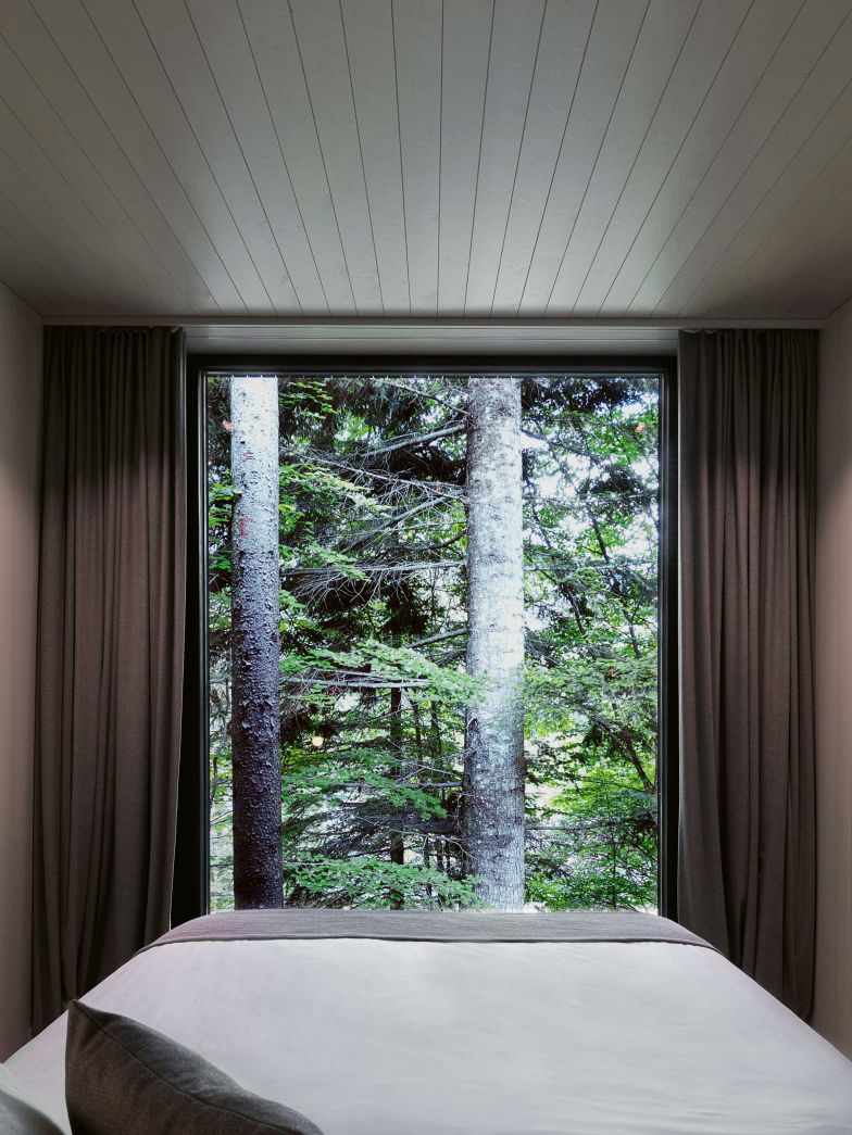 Fensterplatz: Das Bett im Waldhaus steht direkt vor dem grossflächigen Fenster und gibt den Blick frei auf die Bäume und ins Grüne. Foto: Andrea Diglas Photography.